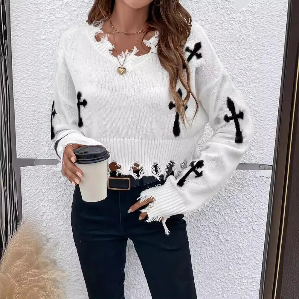 Woman wearing a white sweater with black patterns, holding a coffee cup against a white wall.