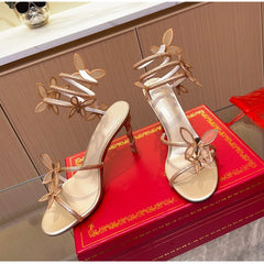 Gold high-heeled shoes with decorative straps on a red box against a wooden cabinet background.