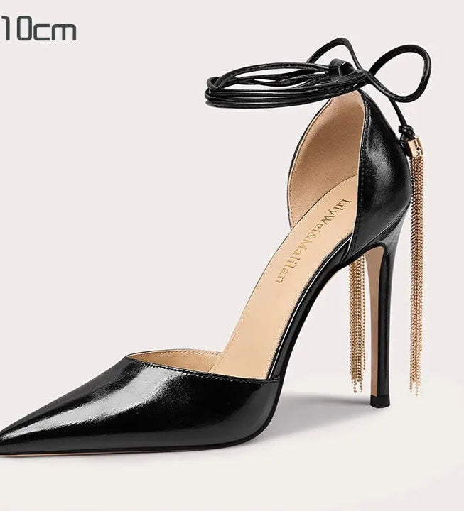 Black high-heeled shoe with gold chain and tassel on a light gray background