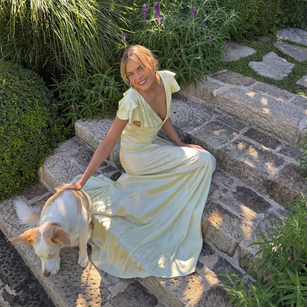 Woman in a light green dress sitting on stone steps with a dog in a garden setting.
