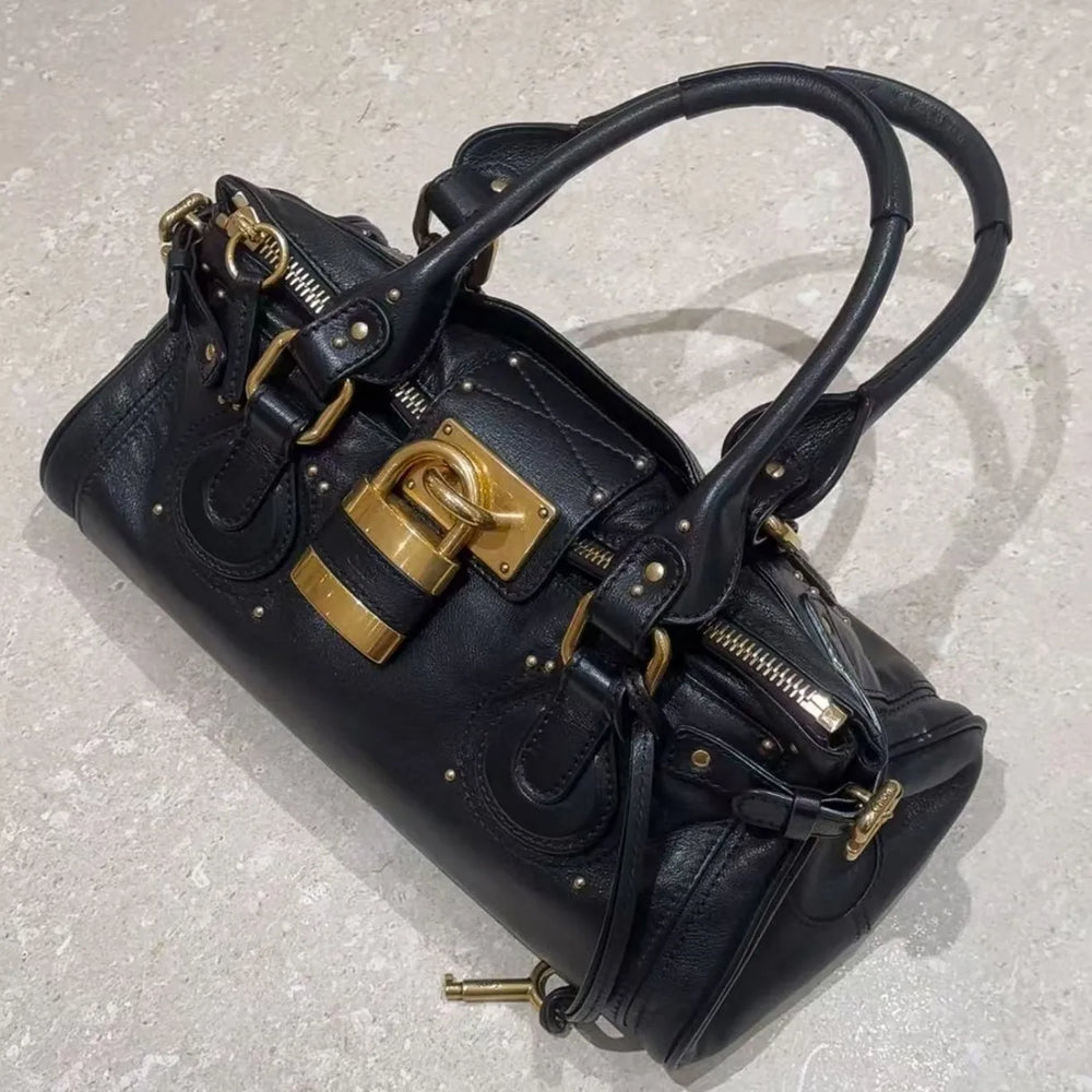 Black leather tote bag with gold lock closure on a textured floor.