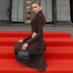 Woman in a brown dress sitting on red steps holding a black handbag.