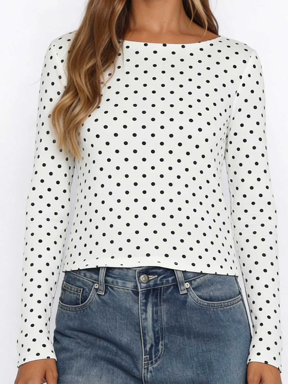 White long-sleeve top with black polka dots worn by a person, paired with blue jeans.