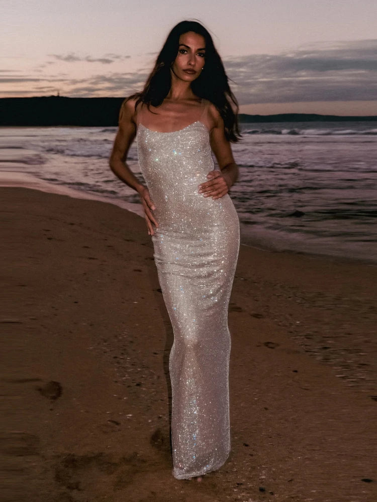 Woman in a sparkly dress standing on a beach at sunset