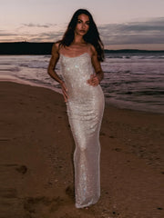 Woman in a sparkly dress standing on a beach at sunset
