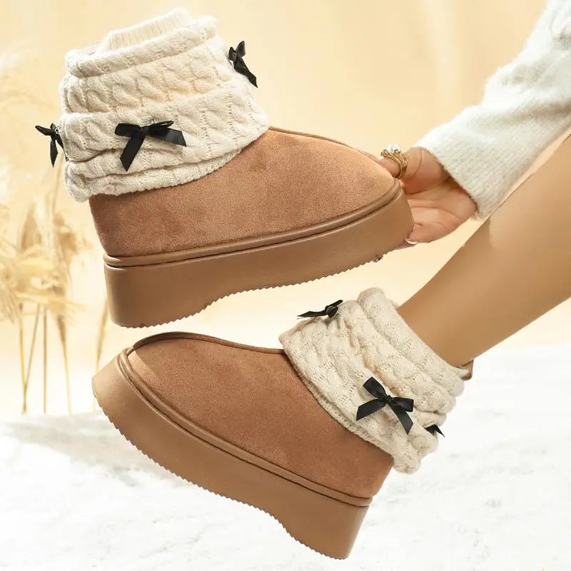 Tan boots with white cuffs and black bows held by a hand against a beige background