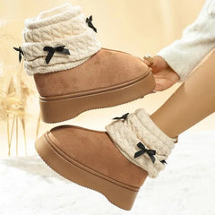 Tan boots with white cuffs and black bows held by a hand against a beige background