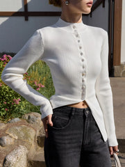 Person wearing a white ribbed sweater with buttons outdoors.