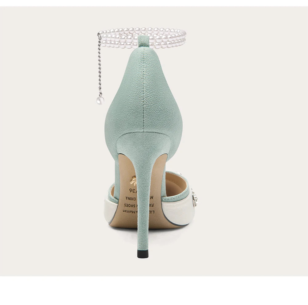 Mint green high-heeled shoes with a pearl anklet on a light gray background