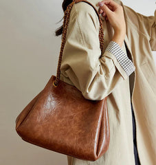 Brown leather handbag held by a person wearing a beige coat against a neutral background