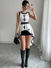 A woman is taking a mirror selfie wearing a black and white dress with a high-low hemline, black knee-high boots, and holding a black handbag.