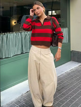 Woman wearing a red and brown striped sweater and beige pants standing on a street.
