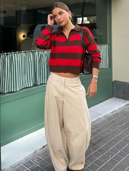 Woman wearing a red and brown striped sweater and beige pants standing on a street.
