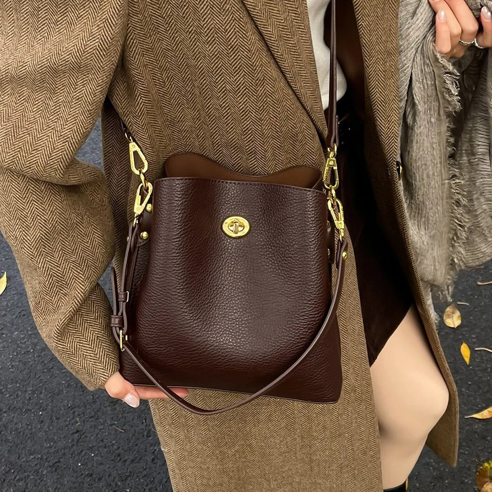 Brown leather handbag with gold accents held by a person wearing a brown coat.