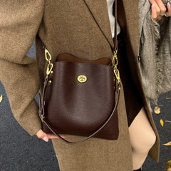 Brown leather handbag with gold accents held by a person wearing a brown coat.