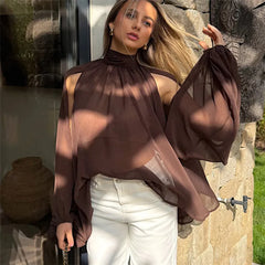 Woman wearing a sheer brown top and white pants outdoors.
