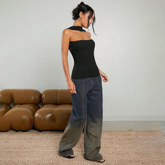 Woman in a black top and blue jeans standing in a room with a brown leather sofa.