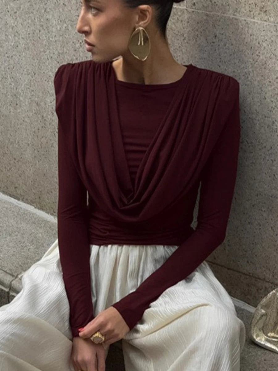 Woman wearing a burgundy top and white skirt against a stone wall.