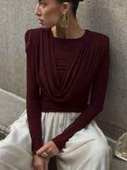 Woman wearing a burgundy top and white skirt against a stone wall.