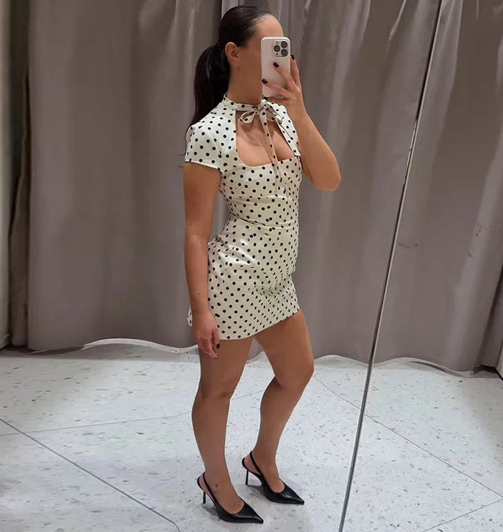 Woman taking a mirror selfie wearing a polka dot dress in a neutral setting