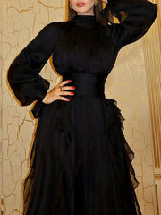 Woman wearing a black dress with long sleeves and ruffled details against a decorative wall.