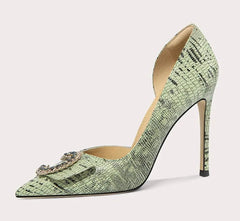 Green high-heeled shoe with a decorative brooch on a light gray background