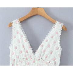 White lace top with pink floral patterns on a wooden hanger against a gray background