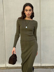 Woman wearing a green ribbed sweater and skirt set against a plain wall.