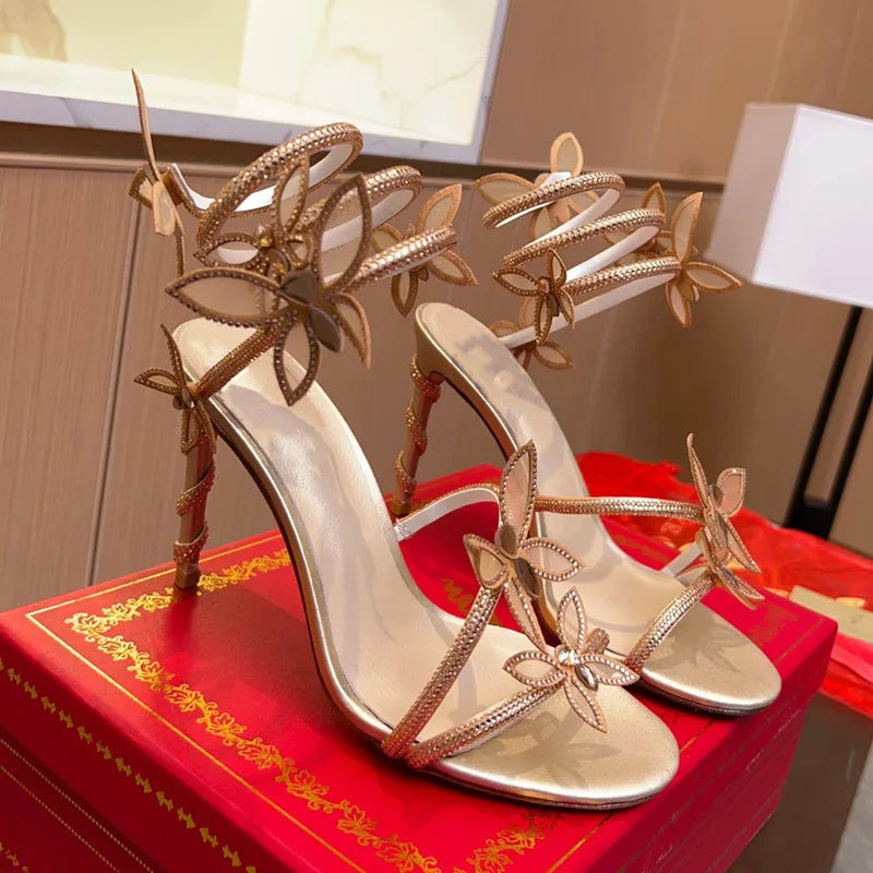 Gold high-heeled sandals with butterfly designs on a red box.