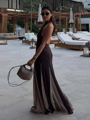 Woman in a long, dark brown dress standing in an outdoor setting with lounge chairs and umbrellas.