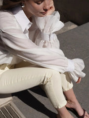 Person wearing a white blouse with ruffled sleeves and light-colored pants sitting on a bench.
