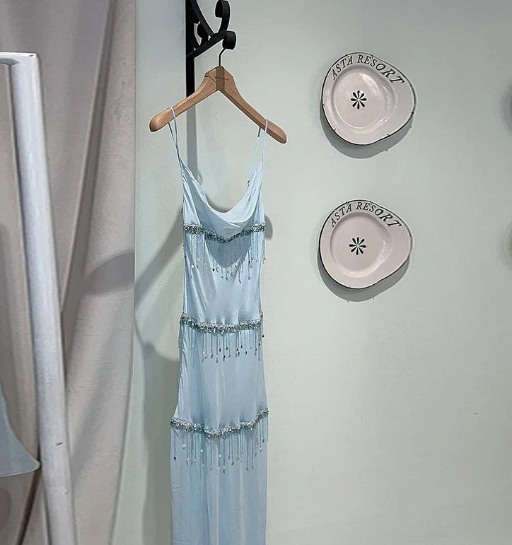 Light blue dress hanging on a wooden hanger against a wall with decorative plates.