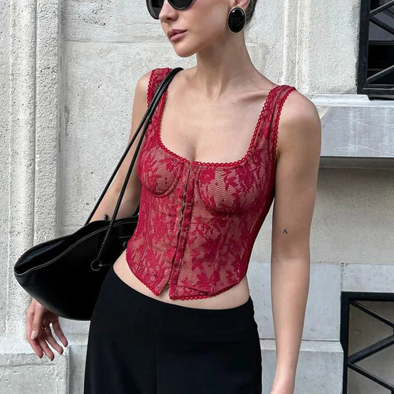 Woman wearing a red lace top and black pants against a light-colored wall.