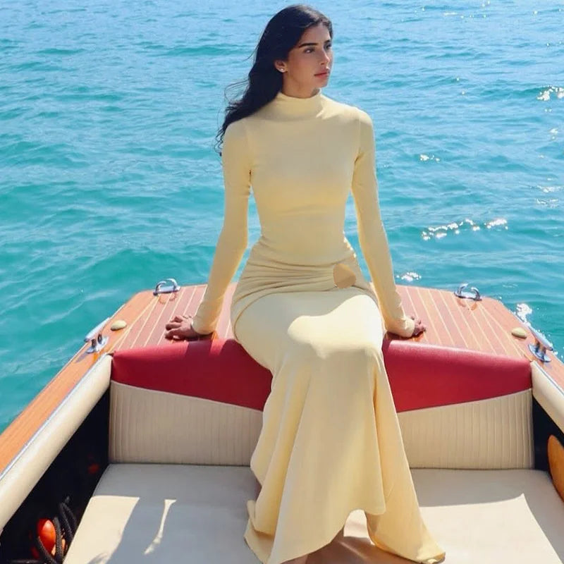 Woman in a yellow dress sitting on a boat with blue water in the background