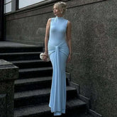 Woman in a light blue dress standing on stone steps against a gray wall.