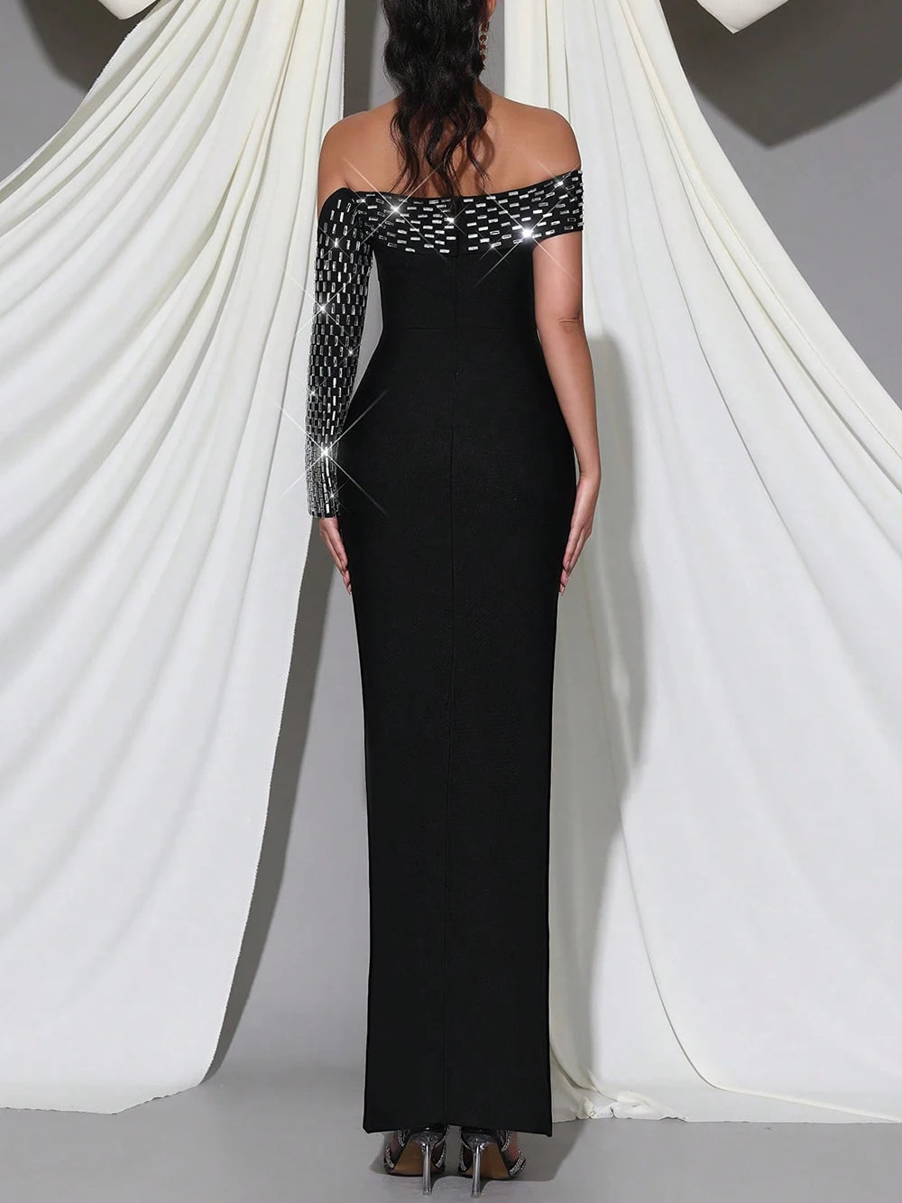 Black evening gown with long sleeves and sequin details on a white draped background