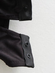 Close-up of a black bodysuit with buttons on a light grey background