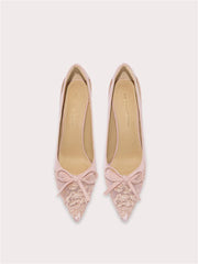 Pair of pink pointed-toe shoes with lace details and bow accents on a light gray background.