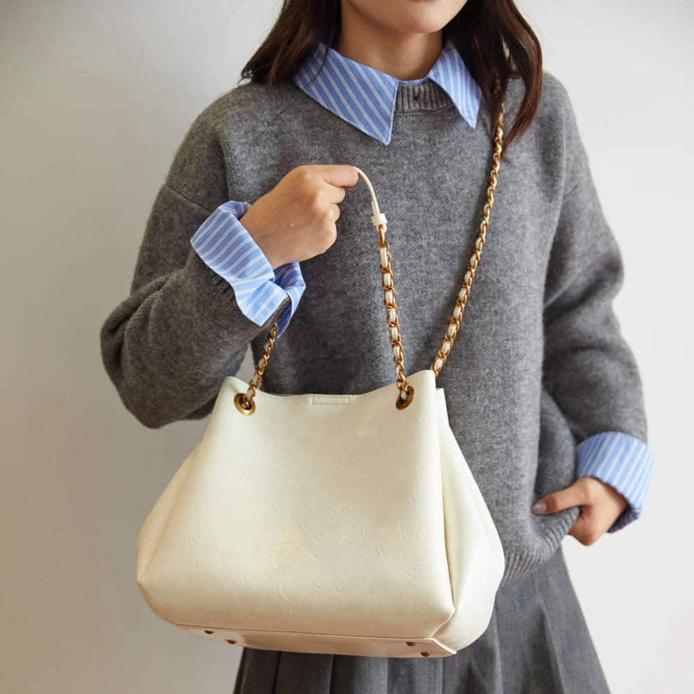 Person wearing a gray sweater with a blue collar holding a cream handbag.
