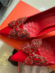 Red high-heeled shoes with decorative bow on a textured surface