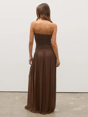 Woman wearing a brown strapless gown against a white wall.