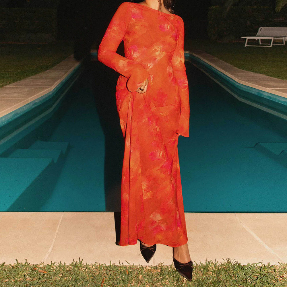Person wearing an orange floral dress standing by a pool at night.