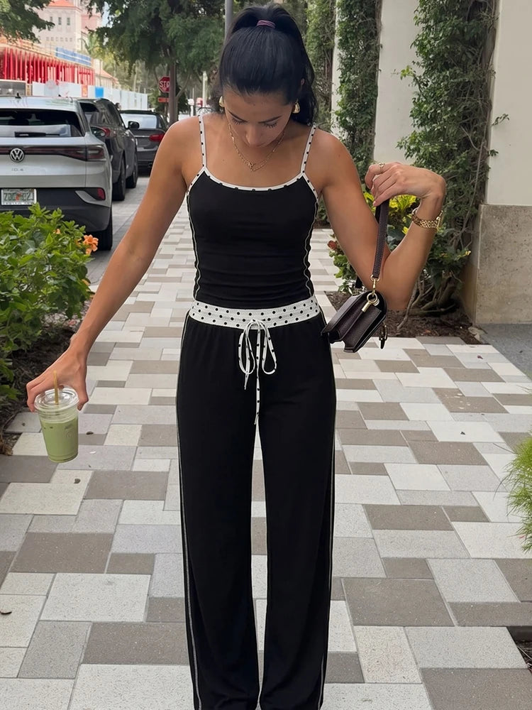 Woman in black camisole top and wide-leg pants set with polka dot trim holding a drink