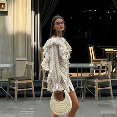 Woman in a white dress with ruffles standing outdoors near tables and chairs.