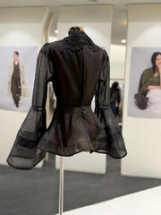 Black sheer blouse on a mannequin in an indoor setting with blurred background