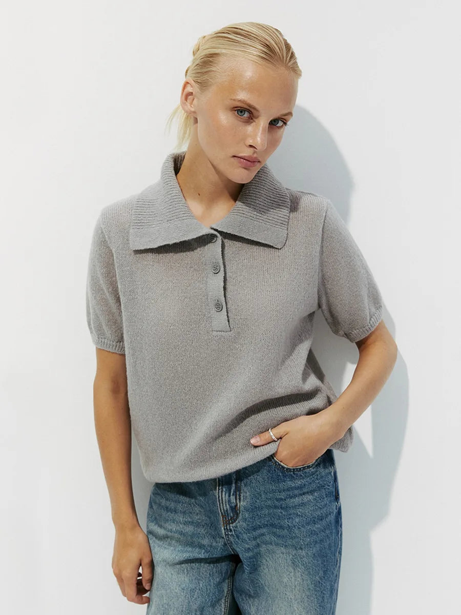 A woman wearing a grey top with a collar and blue jeans on a white background