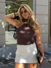 Woman wearing a polka dot top and white skirt outdoors.