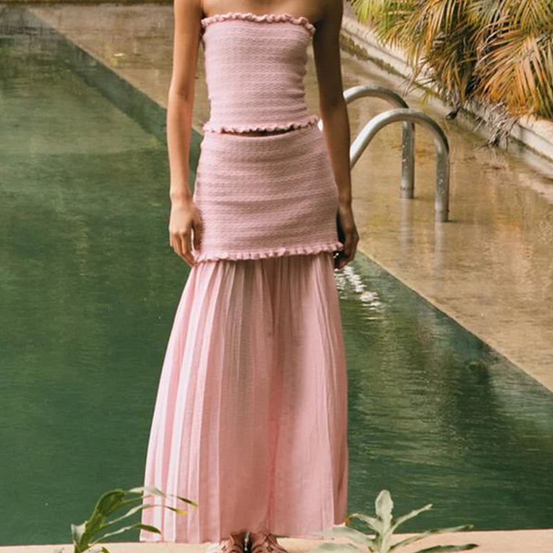 Person wearing a pink dress standing by a pool with greenery in the background