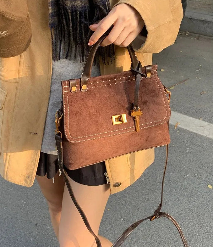 Brown handbag held by a person wearing a beige coat on a street.