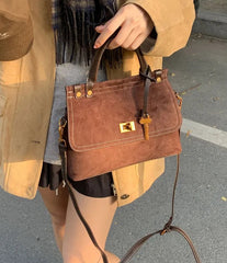 Brown handbag held by a person wearing a beige coat on a street.